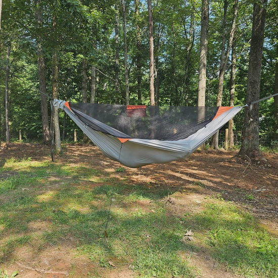 A REM camping hammock with bug net hung between trees