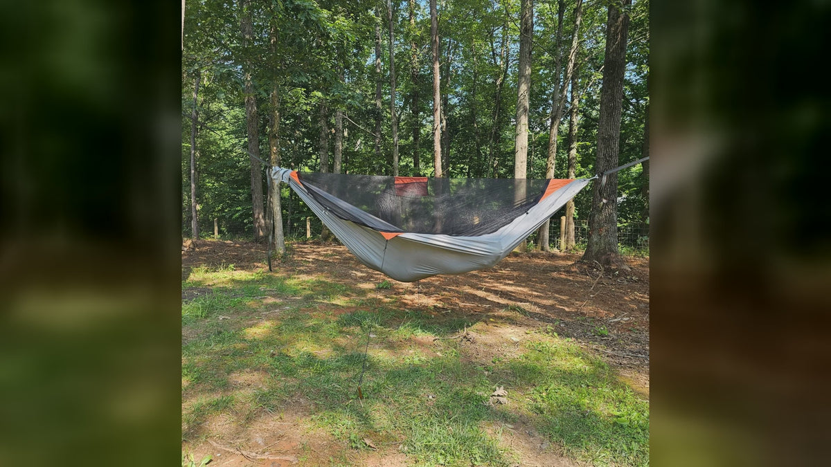 A REM camping hammock with bug net hung between trees